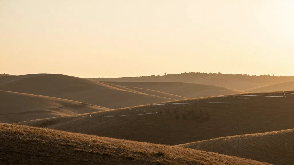 Wide horizon of rolling hills at sunrise, subtle ribbon of finish-line tape across the mid-ground