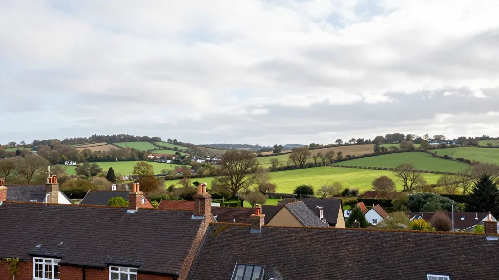 Wide-angle shot of a peaceful countryside valley seen from a loft-conversion vantage point, British rooftops in the foreground