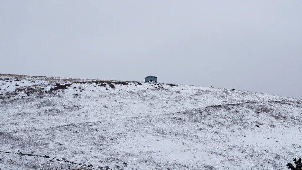 Distant view of a snow-dusted hillside with a single insulated attic hatch visible on the roofline