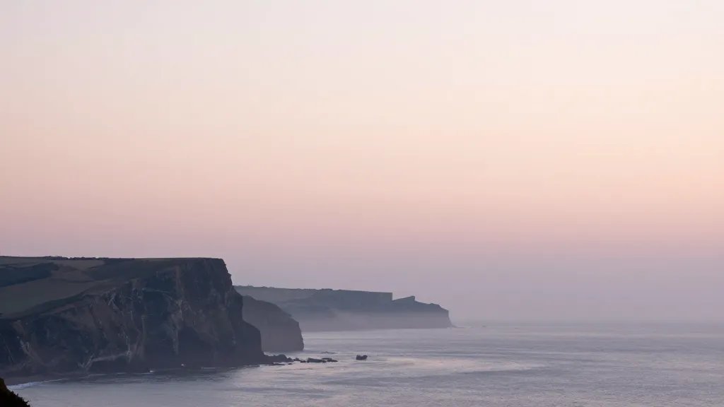 Distant landscape of a misty coastal cliffs at dawn, soft pastel sky
