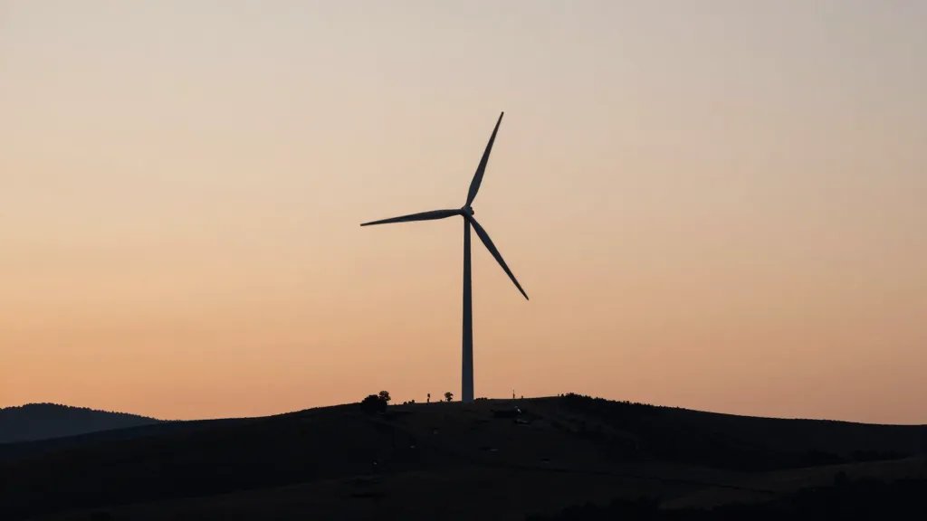 Distant hillside at dusk with a lone wind turbine silhouette