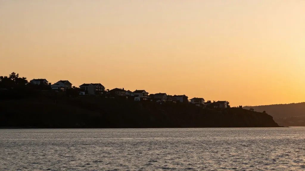 Distant shoreline hillside housing silhouettes at golden hour