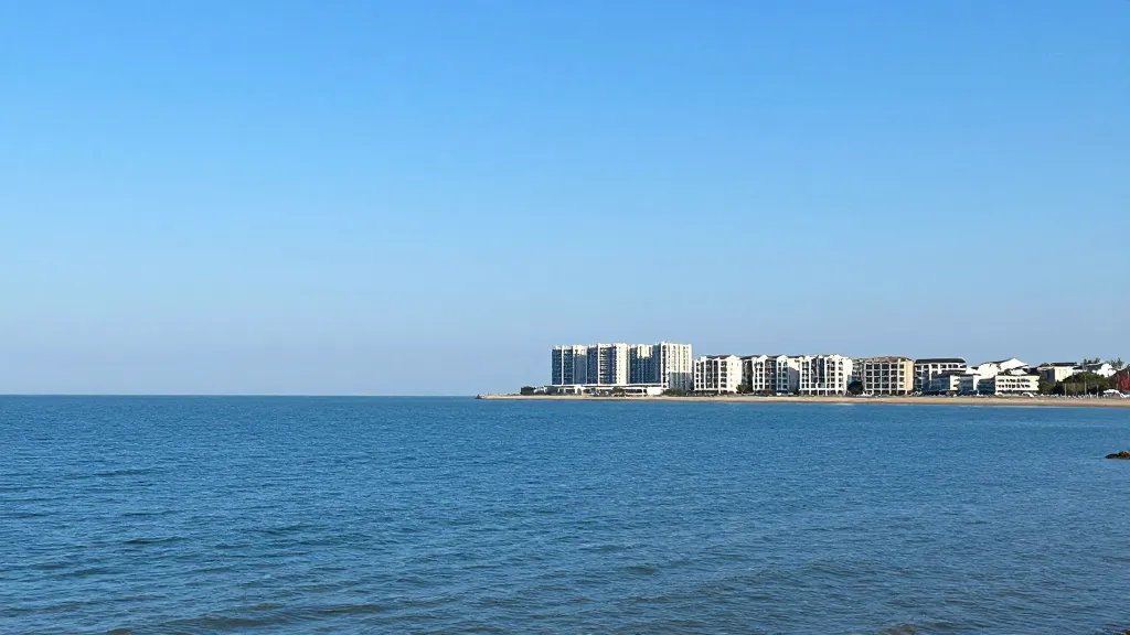 Wide remote coastline with a modern housing development in the mid-distance and clear blue sky