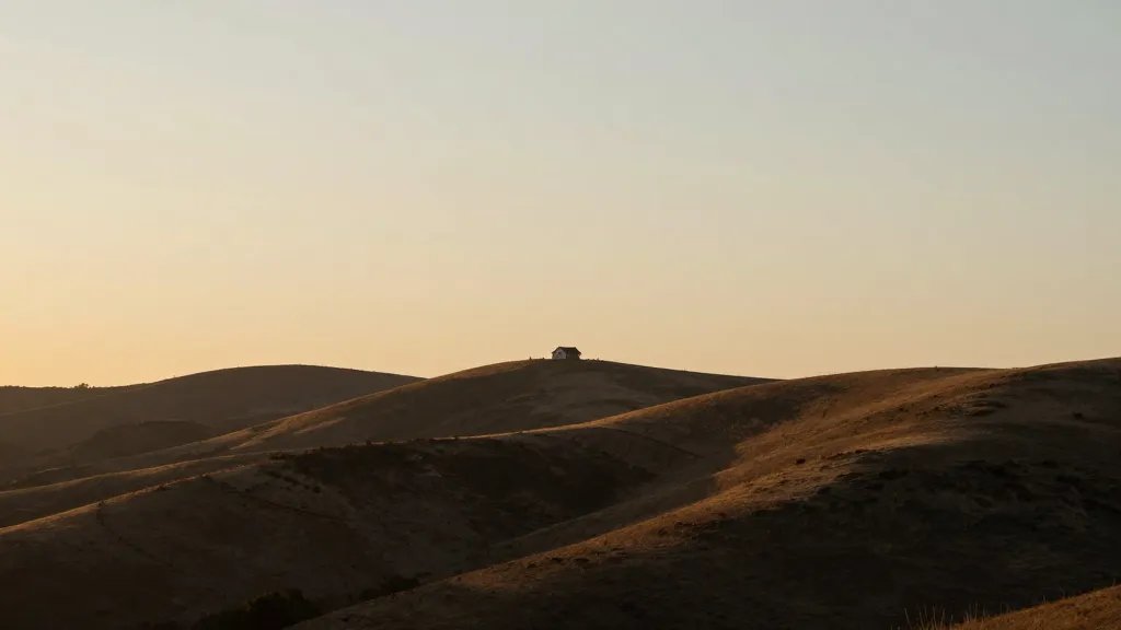 Distant hillside with a lone house on a gentle slope, sunset light