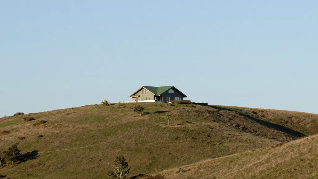 distant hillside with a modern green-roofed home under clear sky