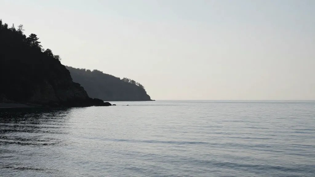 Quiet seaside cliff over calm water, distant coastline silhouette