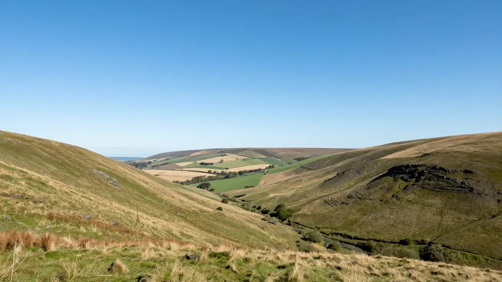 Expansive hillside valley with distant rolling fields under blue skies