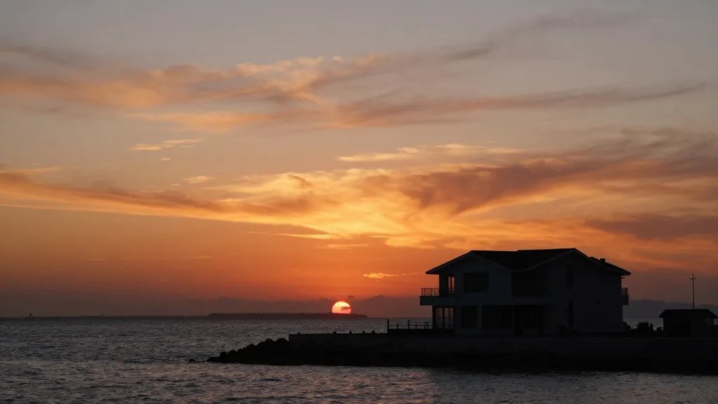 A solitary modern house silhouette against a dramatic harbor sunset