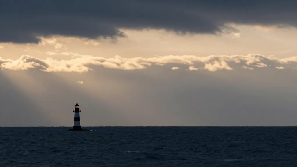 Distant coastal shoreline under dramatic sky, single lighthouse silhouette