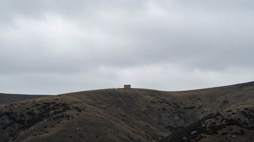 Wide mountain valley from afar, solitary cabin on ridge line