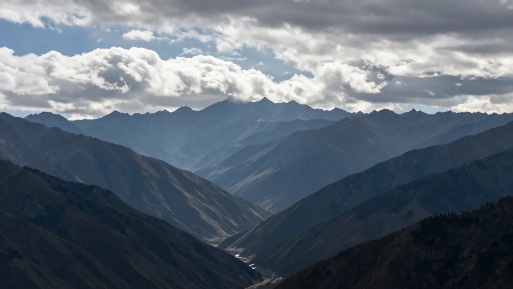 Wide shot of a majestic mountain range, distant peak under dramatic clouds, single subject with expansive valley