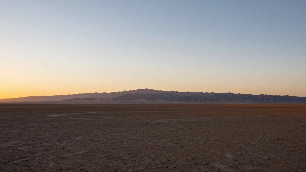 Wide desert plain with distant mountain range at sunset