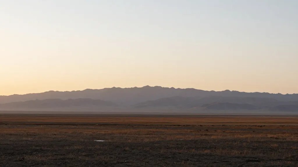 Expansive plain with distant mountain range and soft sunset glow