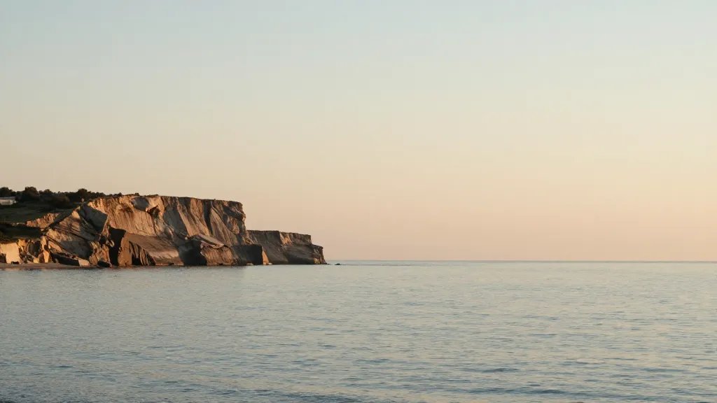 Expansive coastline cliff at golden hour with calm sea, minimalist landscape, no structures