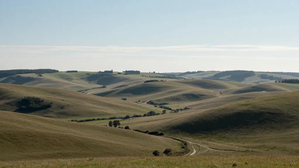 Expansive valley landscape with rolling fields, distant farmhouse silhouettes