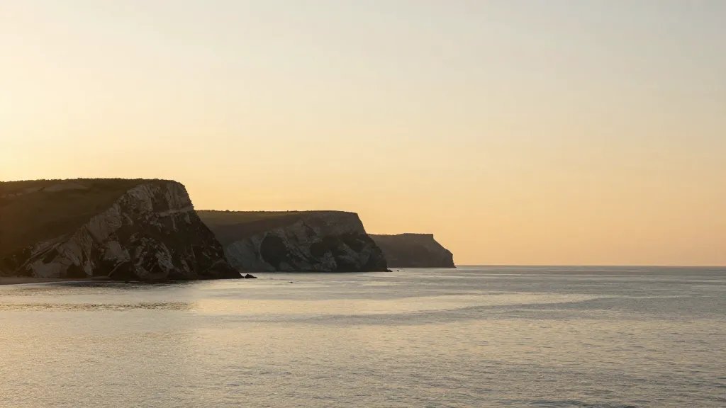 distant coastal cliff landscape at sunrise, calm sea, golden light