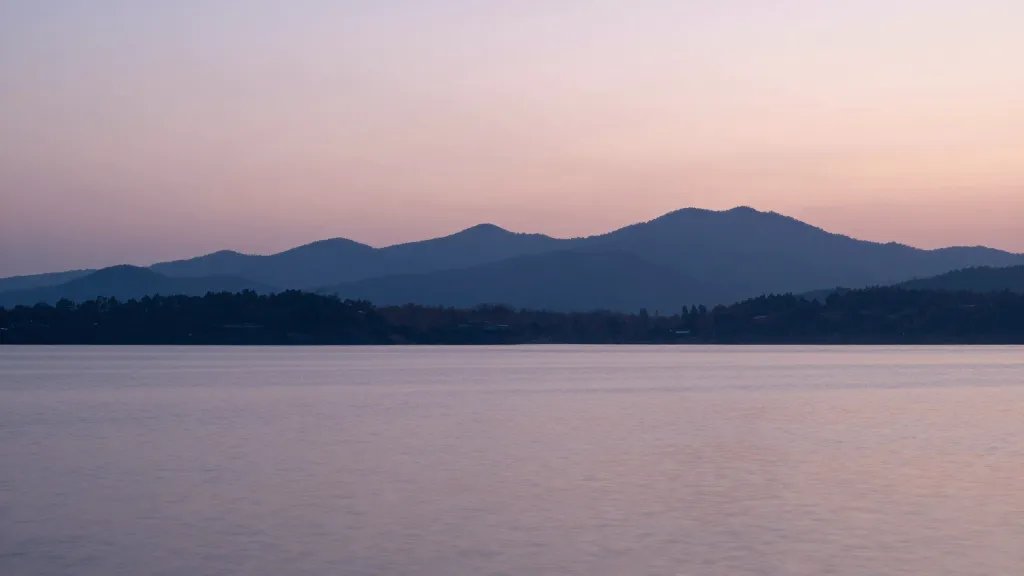 distant mountain silhouette above tranquil lake, soft pastel sky at dusk