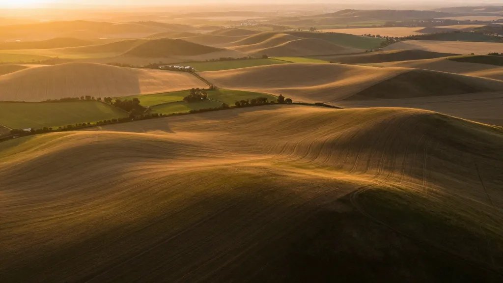 Aerial shot of a rolling rural landscape with patchwork fields, golden hour