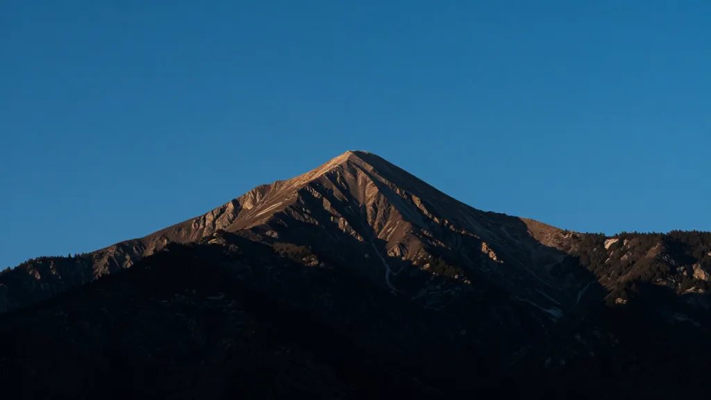 Distant mountain summit under clear blue sky, dramatic alpine lighting
